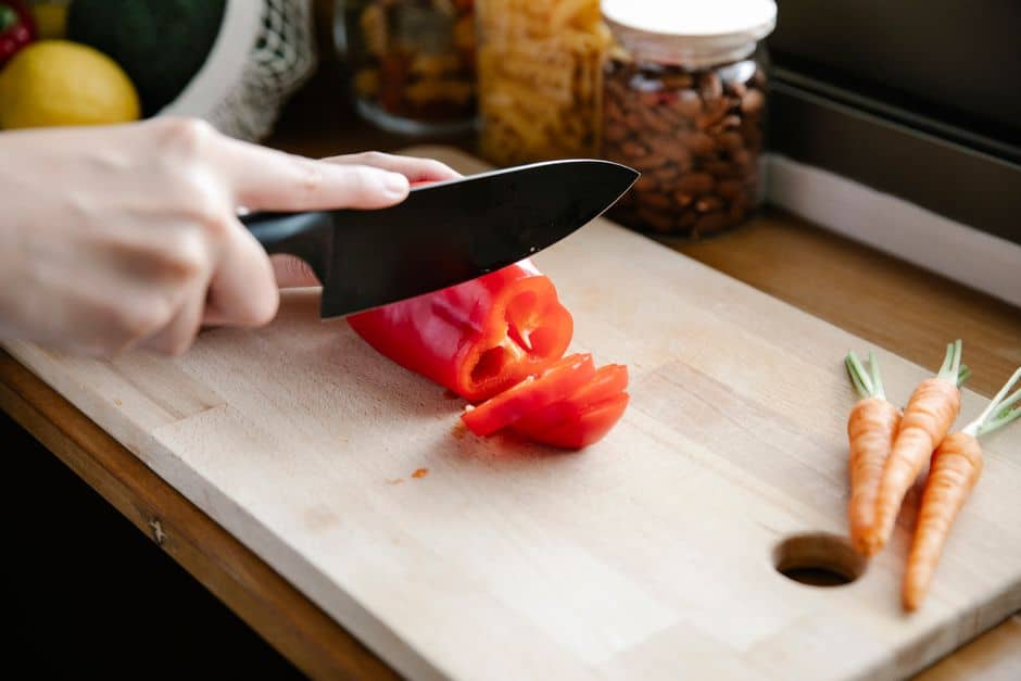 Crop anonymous person slicing ripe fresh red capsicum on chopping board on kitchen counter
